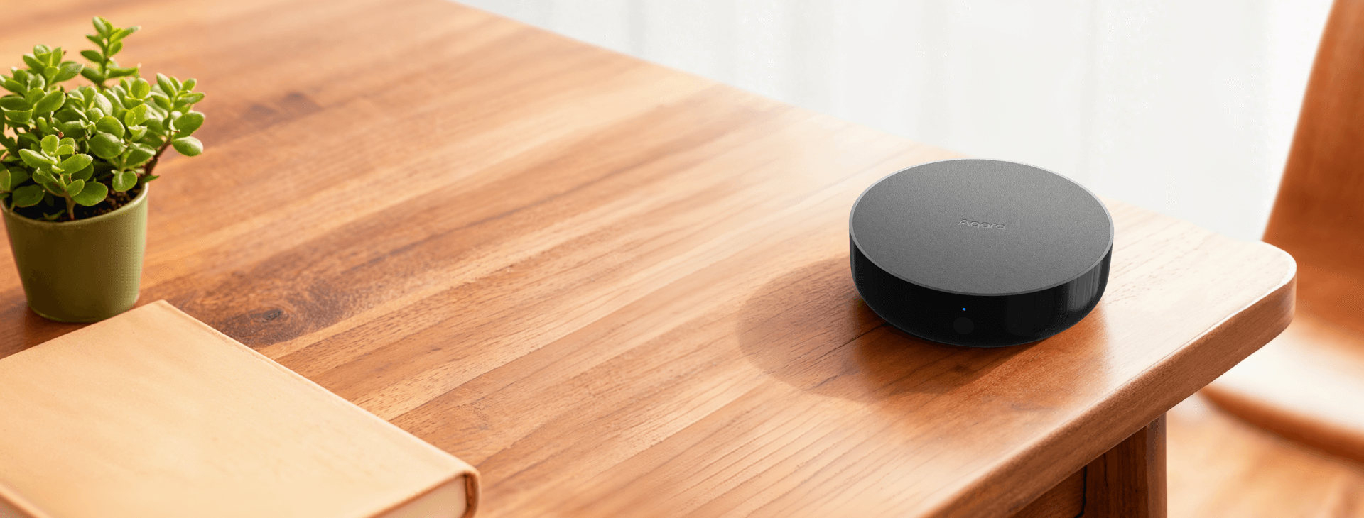 Black Aqara Hub M200 on a warm wooden table in a bright residential room